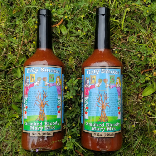 2 bottles of smoked bloody mary mix lying in the grass.